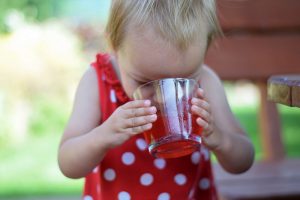 Dieťa v červených šatách s bielymi bodkami, ktoré pije ríbezľovú limonádu