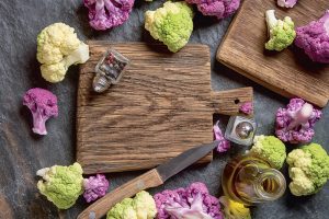 Ružičky fialového a slabozeleného karfiolu na stole s drevenou podložkou na krájanie