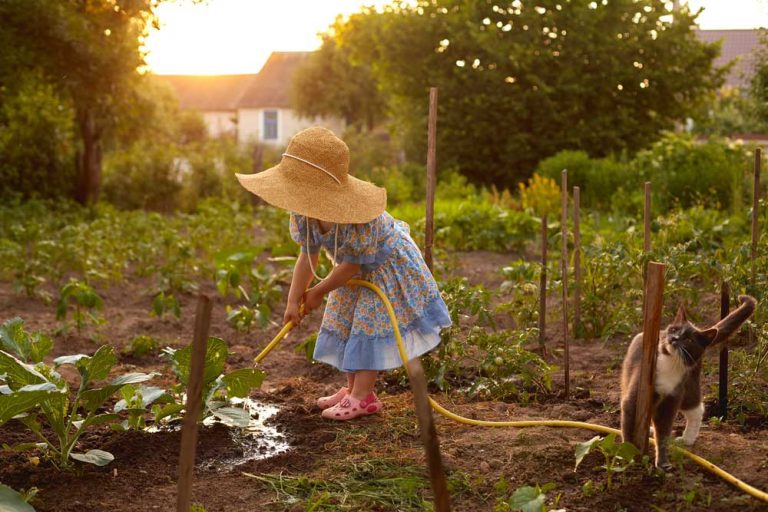 Dievčatko v šatách polieva zeleninu v záhrade