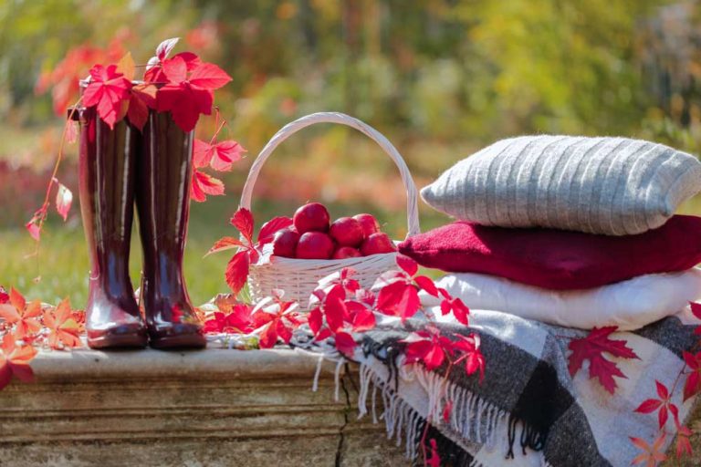 Jesenné zátišie v záhrade, červené gumáky, lístie, vankúše a deky