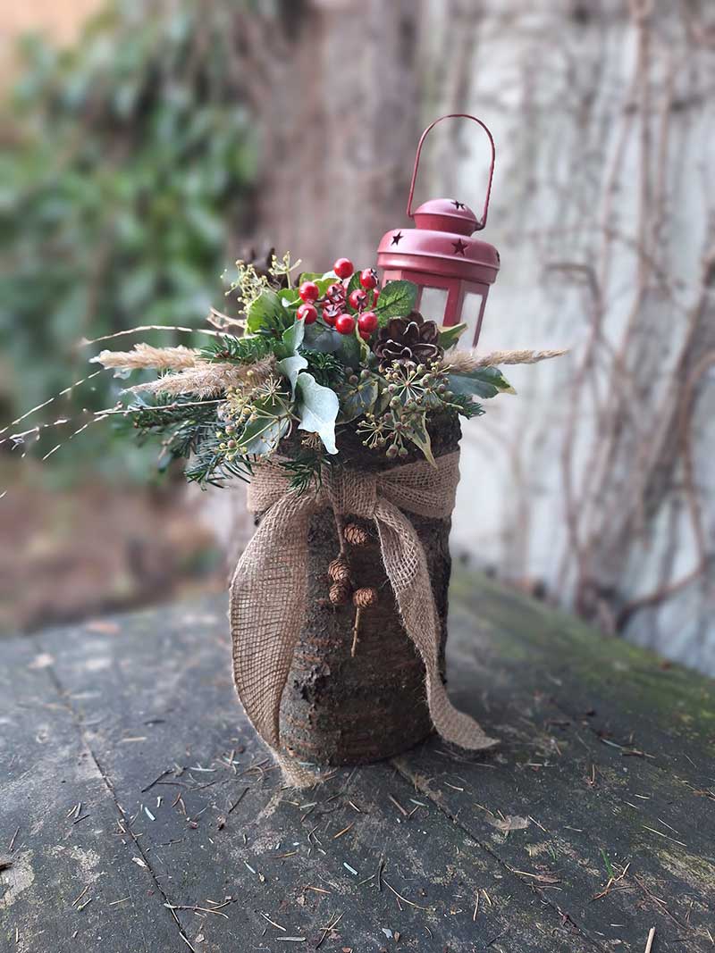 Prírodná zimná dekorácia do záhrady z dreveného polena, okrasných rastlín a malého lampáša
