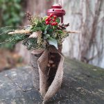 Zimná vonkajšia dekorácia z dreveného polena, čečiny, šišiek, obviazaná jutovou stuhou a dozdobená červeným lampášikom