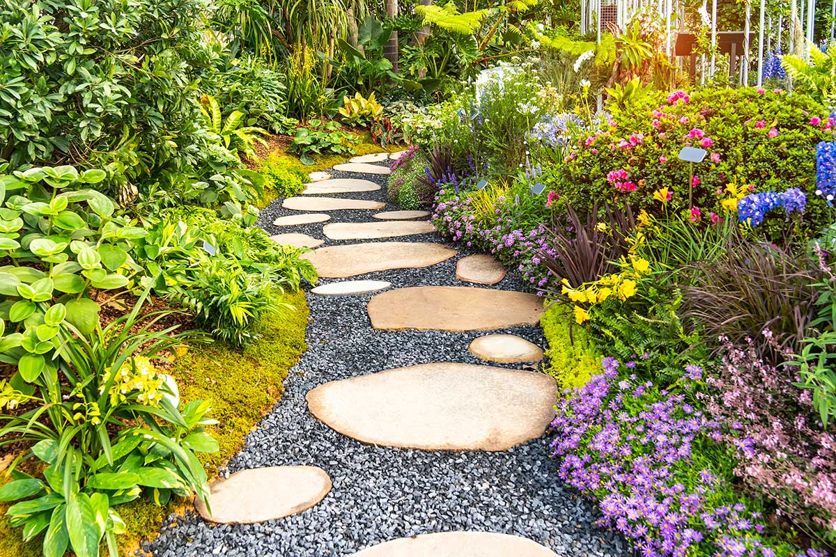 Záhradný chodníček z veľkých kameňov obklopený farebnými kvetmi a bujnou zeleňou