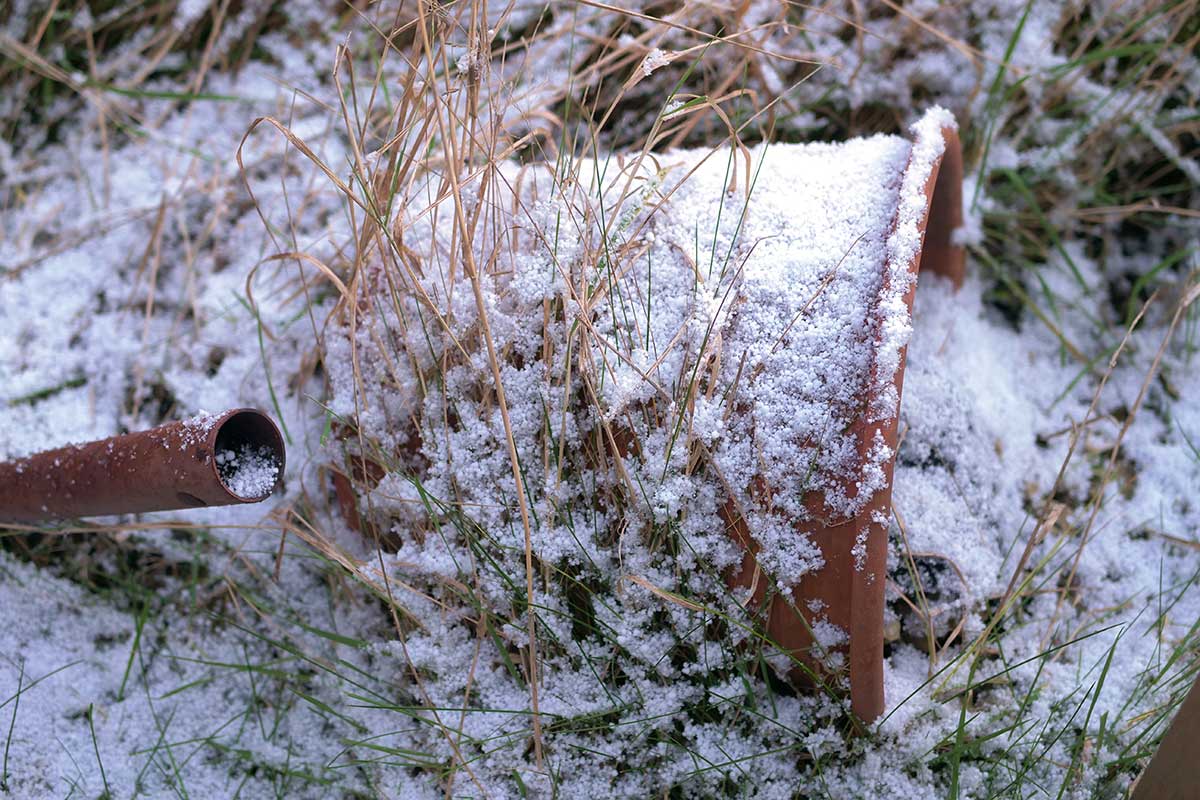 Zamrznutý a snehom zasypaný kvetináč položený na bok