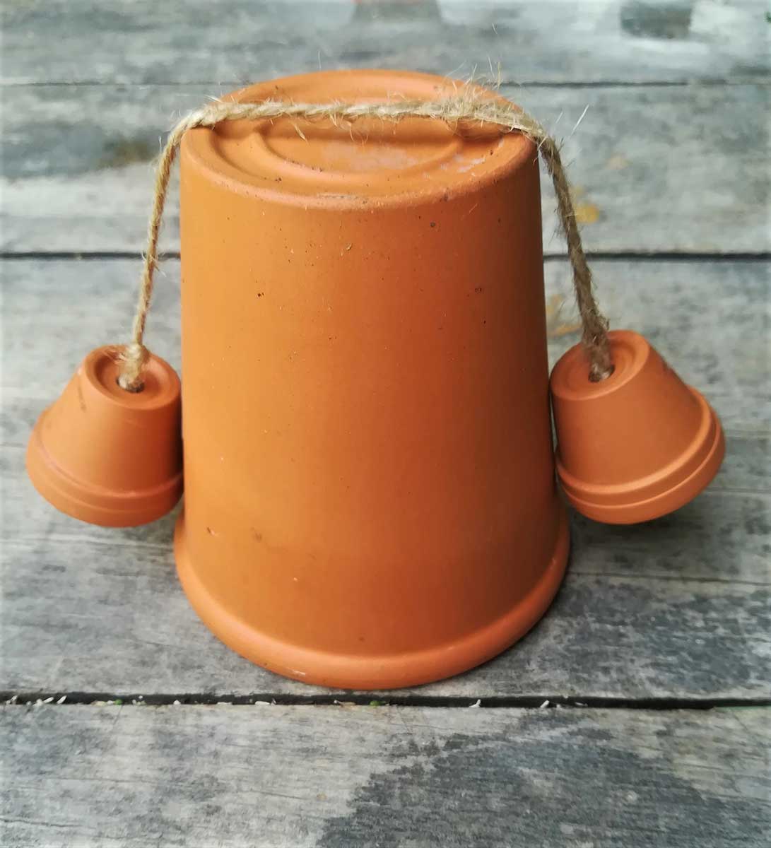 Špagát s rukami preložíme cez prvý veľký črepník, ktorý bude tvoriť telo. 